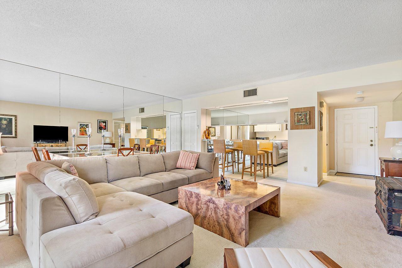 A living room features a large sectional sofa, a burl wood coffee table, and mirrored walls — 11863 Wimbledon Circle # 426, Wellington FL 33414, WELLINGTON, FL