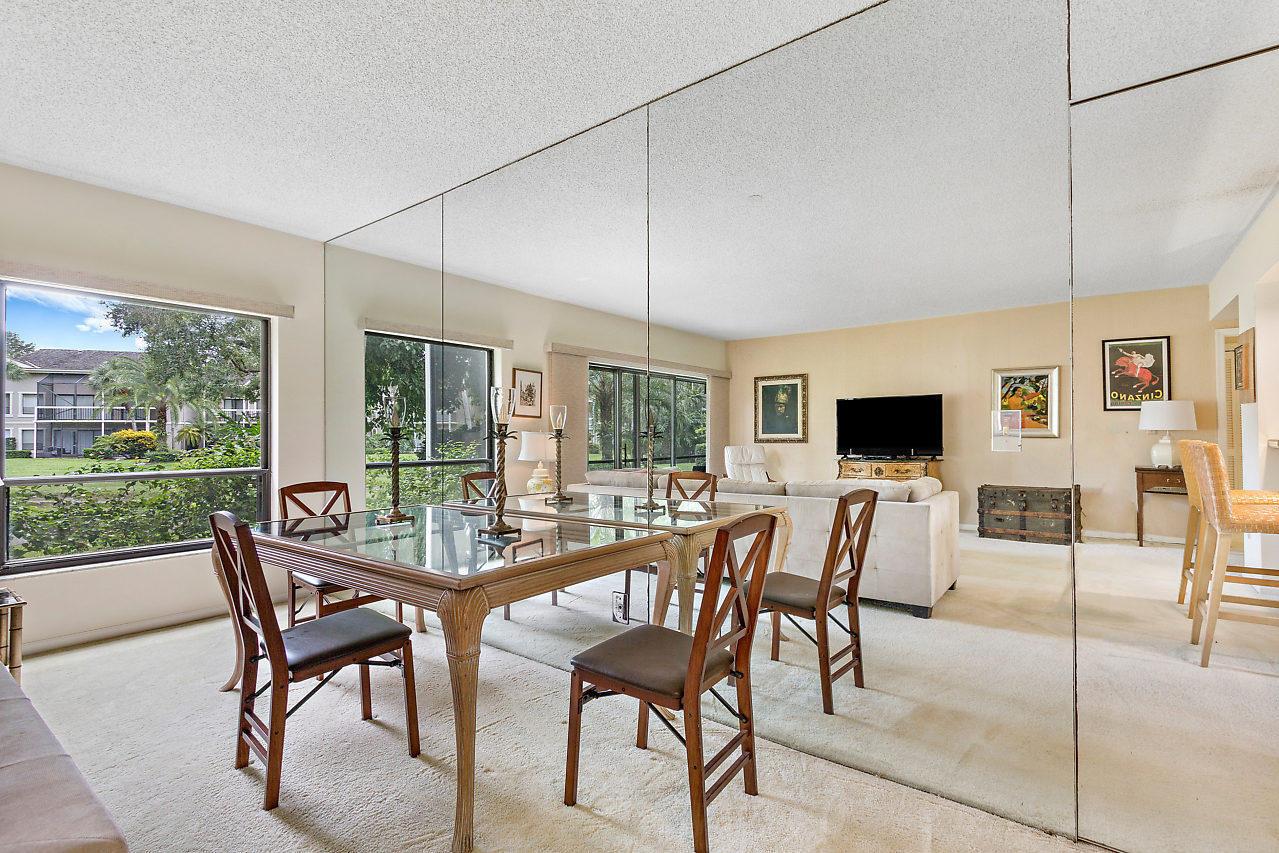 A dining area with a glass table and mirrored wall opens into a living room — 11863 Wimbledon Circle # 426, Wellington FL 33414, WELLINGTON, FL