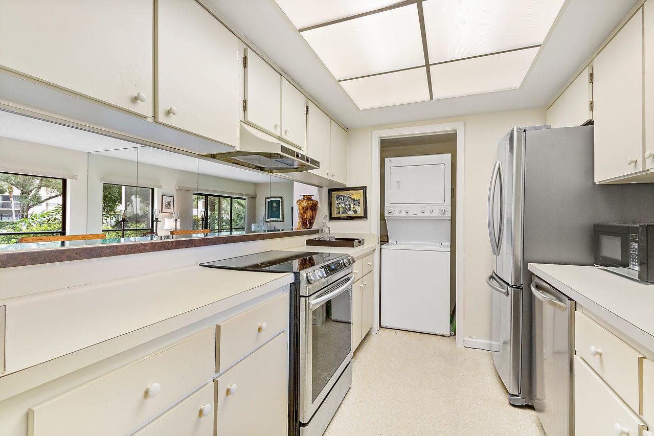 A kitchen with white cabinets, stainless steel appliances, a stacked washer-dryer, and a mirrored backsplash — 11863 Wimbledon Circle # 426, Wellington FL 33414, WELLINGTON, FL