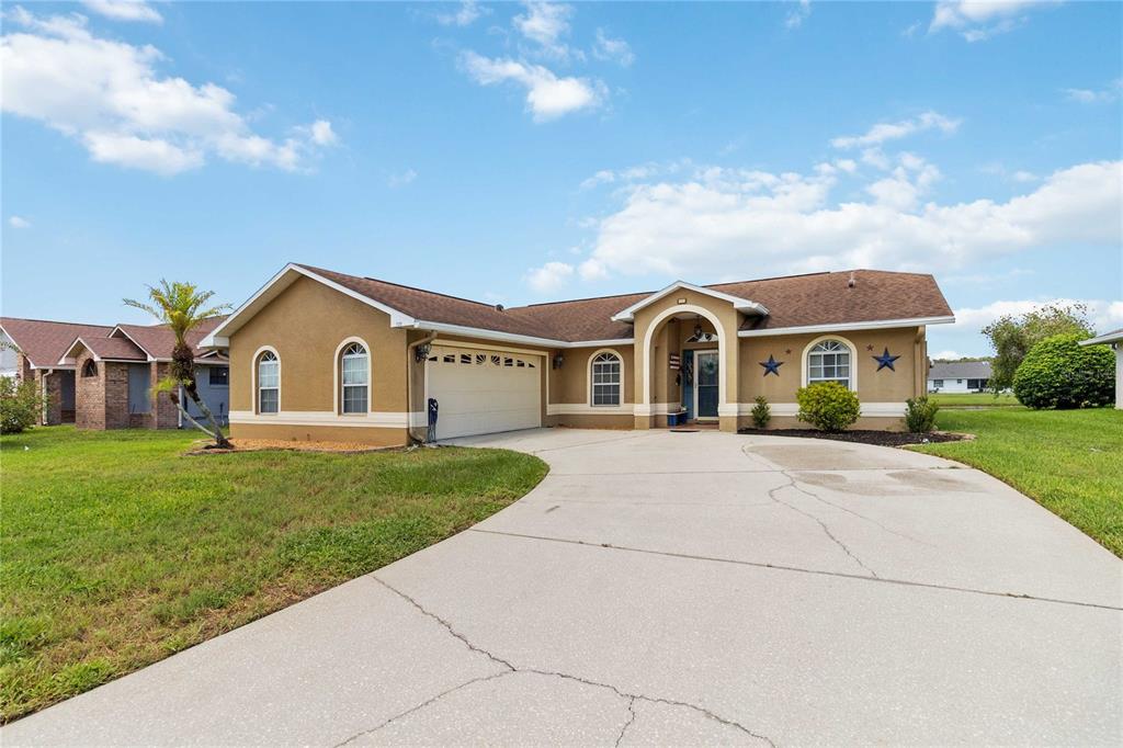 A single-story tan house with a two-car garage and a concrete driveway under a blue sky — 2310 GISELLE COURT, ST CLOUD, FL