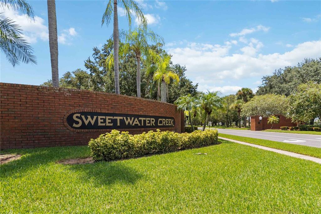 A brick wall with a Sweetwater Creek sign stands beside a road and palm trees — 2310 GISELLE COURT, ST CLOUD, FL