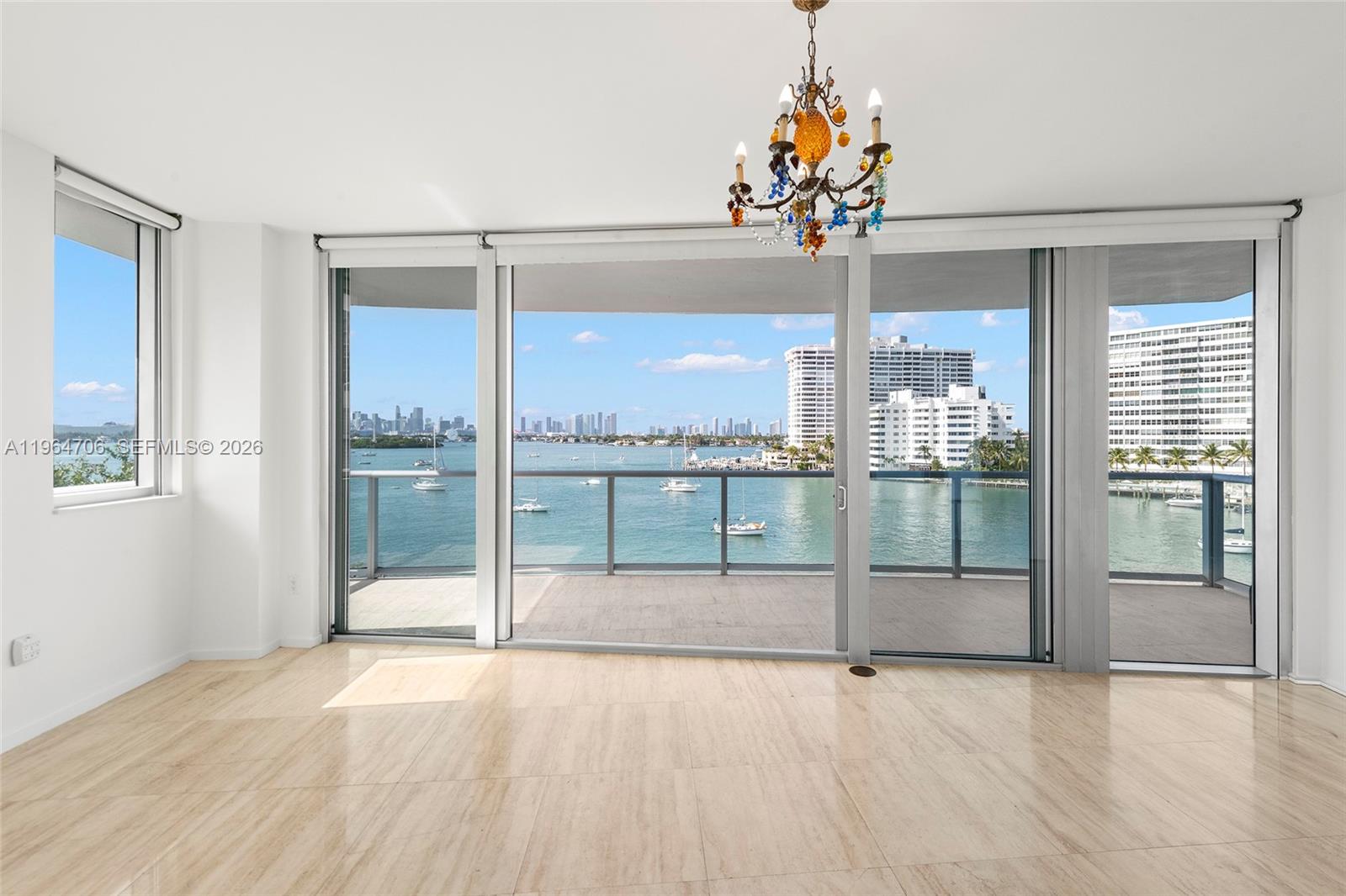 An empty room with light-colored tile flooring, a decorative chandelier, and floor-to-ceiling windows overlooking water — 1470 16th St # 501, Miami Beach FL 33139, MIAMI BEACH, FL