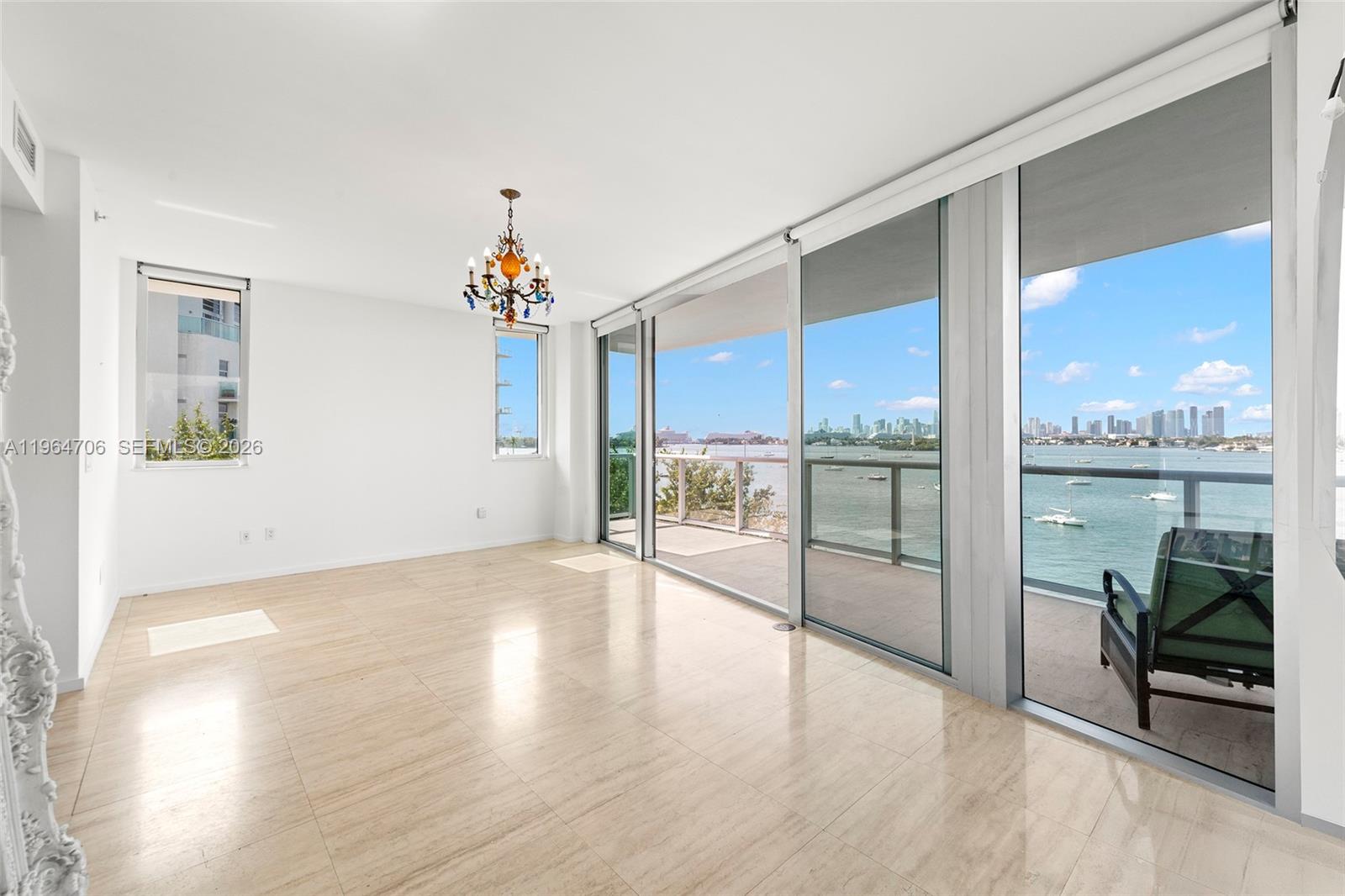 A bright living room features light tile flooring, a colorful chandelier, and floor-to-ceiling balcony windows — 1470 16th St # 501, Miami Beach FL 33139, MIAMI BEACH, FL