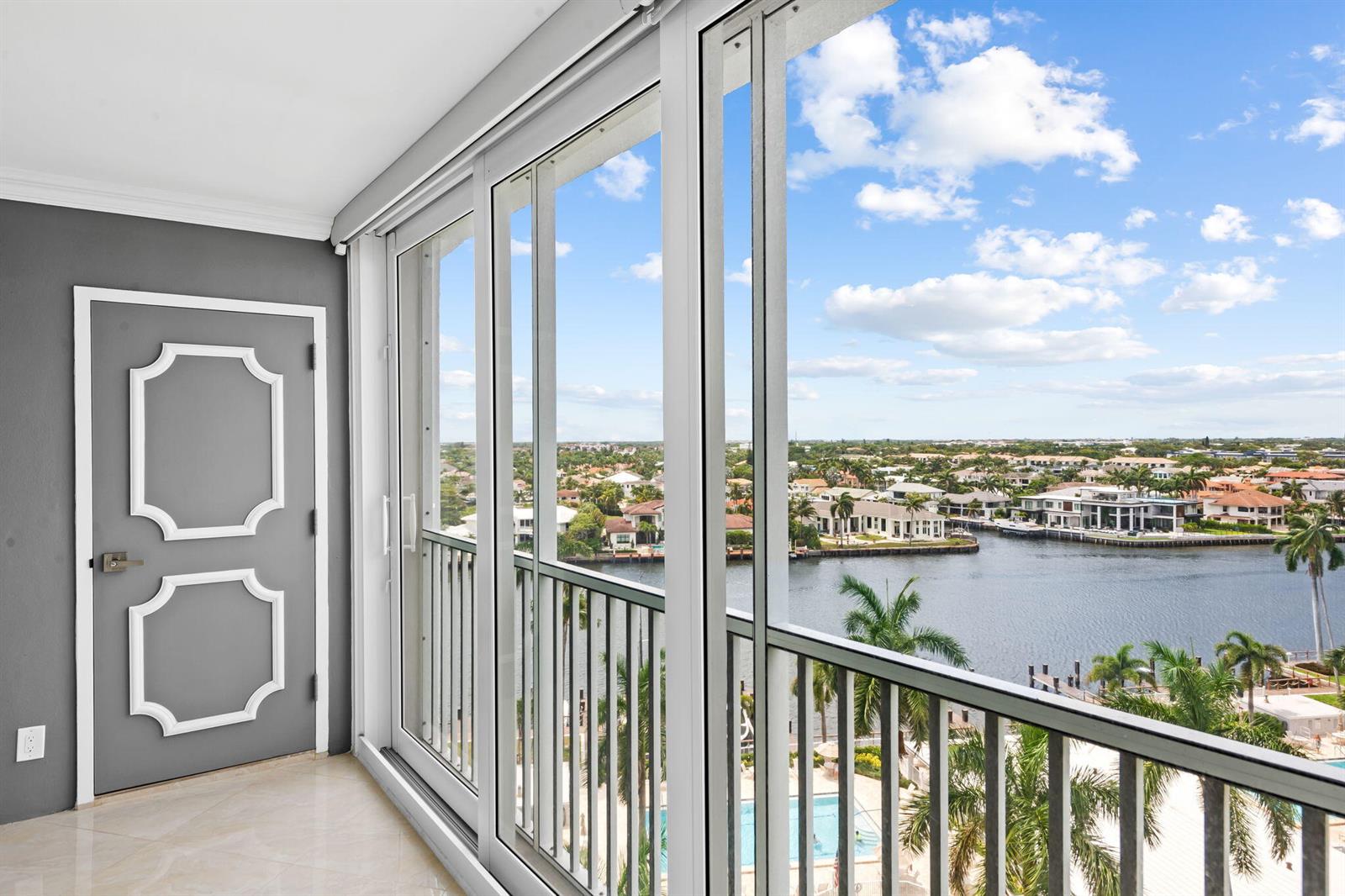 A balcony with sliding glass doors overlooks a canal, palm trees, and residential houses — 3300 S Ocean Boulevard # 1020, Highland Beach FL 33487, HIGHLAND BEACH, FL