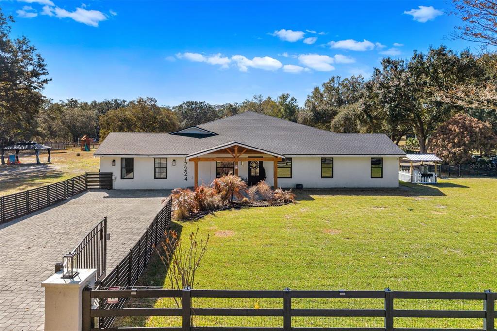 A white single-story house features a dark shingled roof, wooden porch supports, and a paver driveway — 17224 OLD COUNTRY LANE, WINTER GARDEN, FL