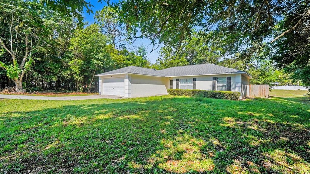 A single-story house with a white exterior, a two-car garage, and a large grassy yard — 56 HEMLOCK RADIAL, OCALA, FL