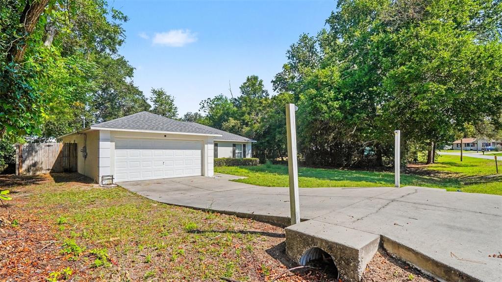 A single-story house with a white garage door and a concrete driveway in a wooded area — 56 HEMLOCK RADIAL, OCALA, FL
