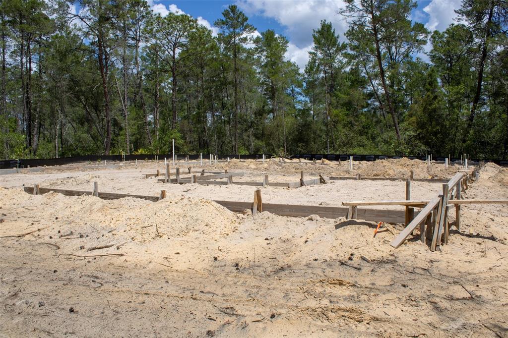A construction site shows a concrete foundation form set in a sandy, wooded lot — 6163 N CANYON DRIVE, BEVERLY HILLS, FL