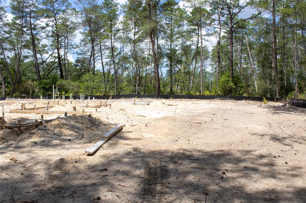 A sandy construction site shows wooden foundation forms and a black silt fence near trees — 6163 N CANYON DRIVE, BEVERLY HILLS, FL