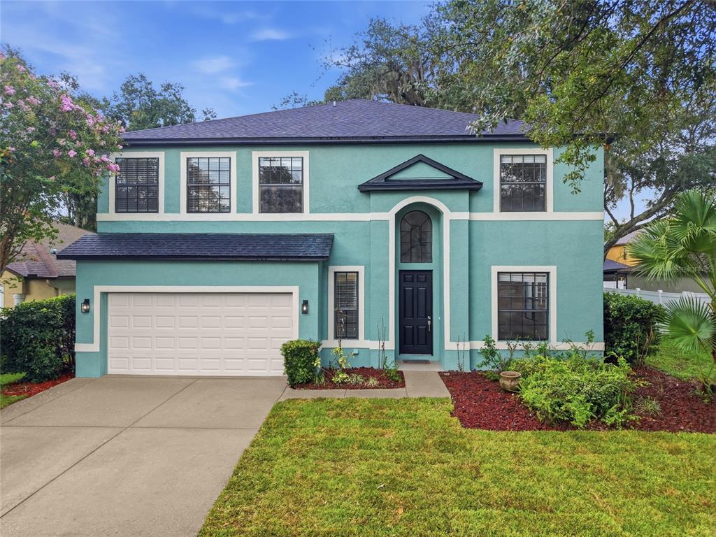A two-story teal house with a white garage door and a dark-colored roof — 1908 ABBEY RIDGE DRIVE, DOVER, FL