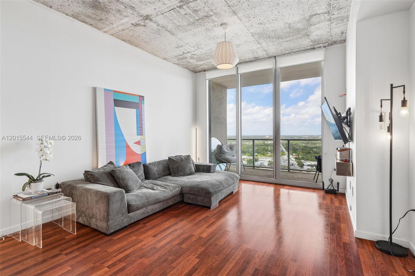 A living room features a grey sectional sofa, concrete ceiling, and floor-to-ceiling windows with views — 3470 E Coast Ave # H2503, Miami FL 33137, MIAMI, FL
