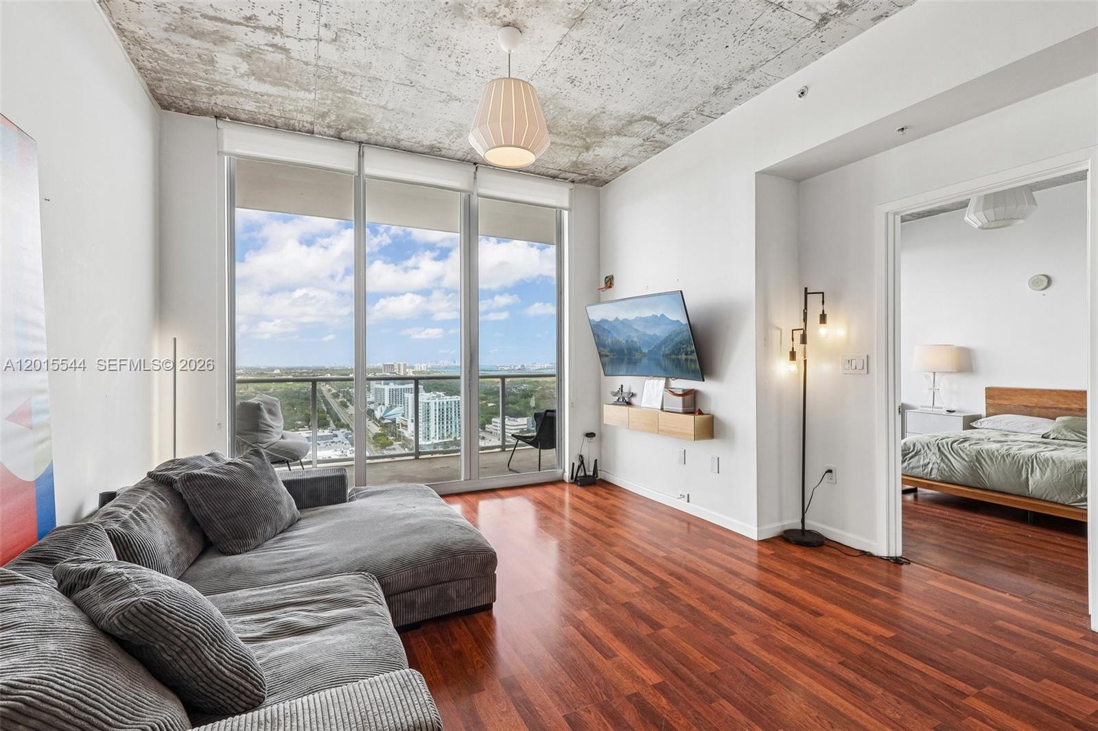 A living room features a grey sectional sofa, wood floors, and a concrete ceiling — 3470 E Coast Ave # H2503, Miami FL 33137, MIAMI, FL