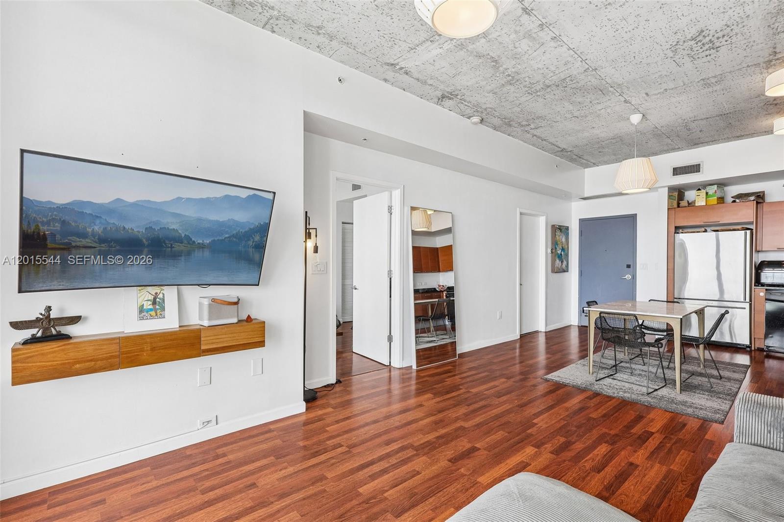 A living and dining area features a concrete ceiling, hardwood floors, and a wall-mounted television — 3470 E Coast Ave # H2503, Miami FL 33137, MIAMI, FL