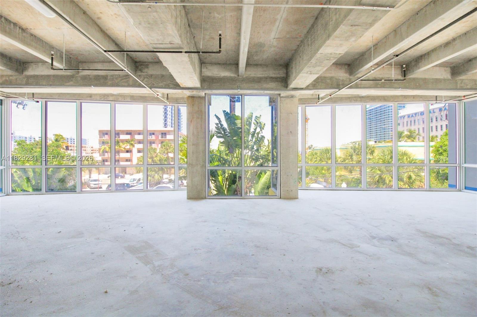 An unfinished interior space features exposed concrete ceilings, support columns, and floor-to-ceiling windows — 6936 Collins Ave, Miami Beach FL 33141, MIAMI BEACH, FL