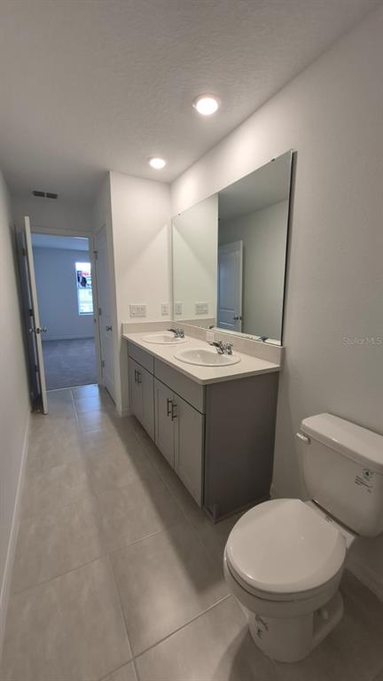 A bathroom features a double-sink vanity with gray cabinets, a large mirror, and tile flooring — 2860 SKYLINE LOOP, KISSIMMEE, FL