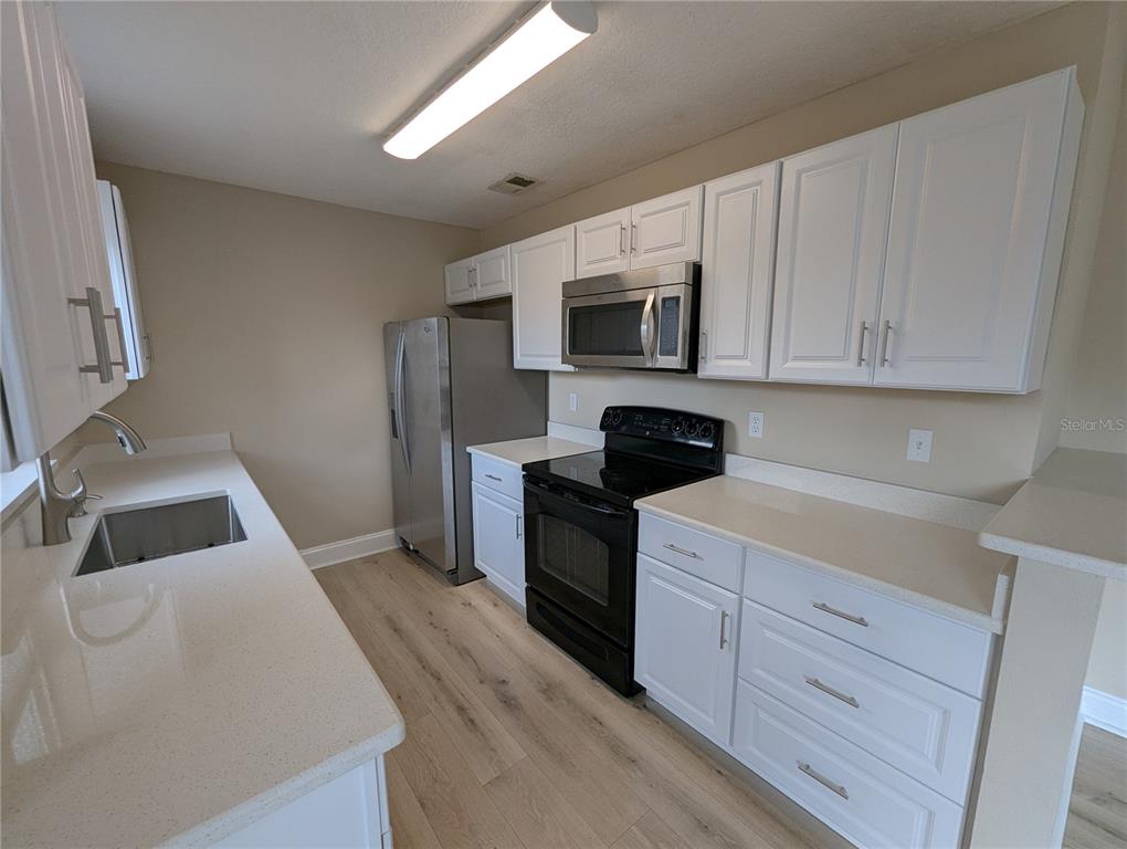A kitchen features white cabinets, stainless steel appliances, a black stove, and light wood flooring — 1209 MOHRLAKE DRIVE, BRANDON, FL