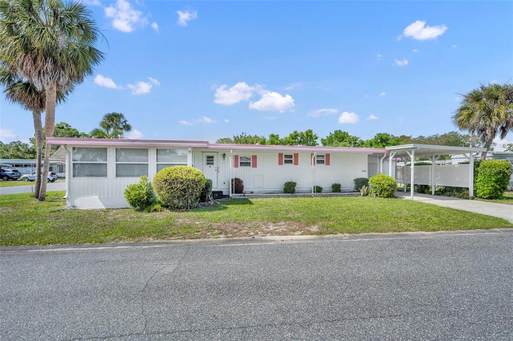 A single-story mobile home with white siding, red shutters, and an attached carport — 270 PALAI AVENUE, LEESBURG, FL