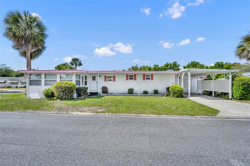 A single-story mobile home features white siding, red shutters, and an attached carport — 270 PALAI AVENUE, LEESBURG, FL