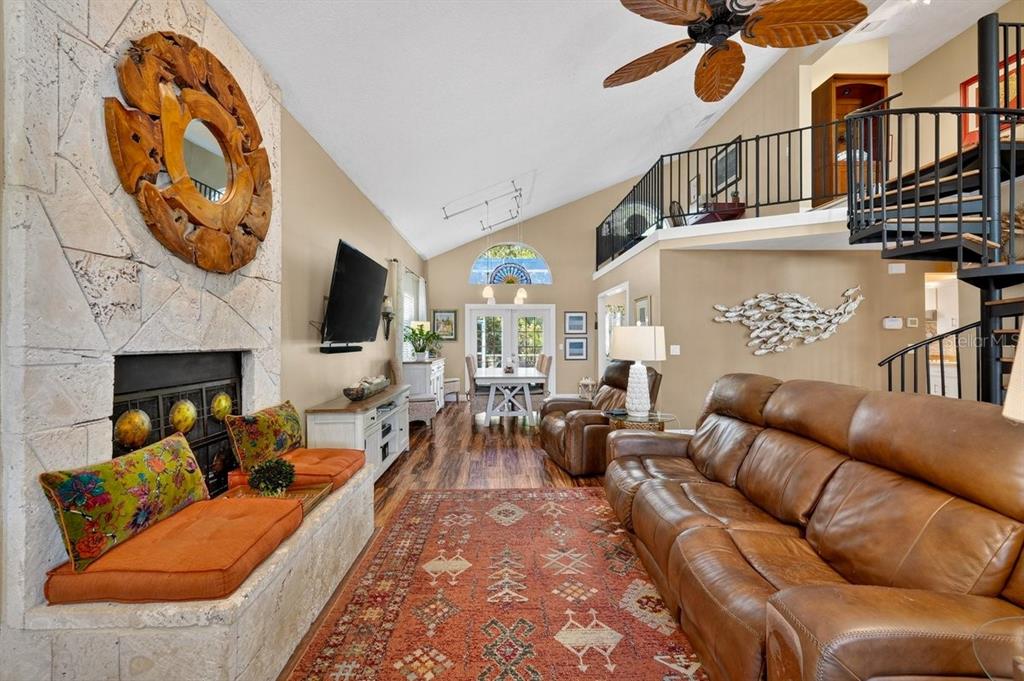 A living room features a stone fireplace, leather sofa, wood floors, and a spiral staircase — 4758 S PENINSULA DRIVE, PONCE INLET, FL