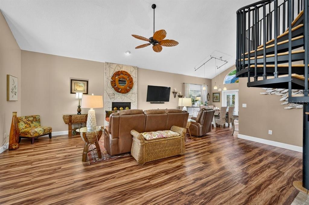 A living room features wood-look flooring, a stone fireplace, and a black spiral staircase — 4758 S PENINSULA DRIVE, PONCE INLET, FL