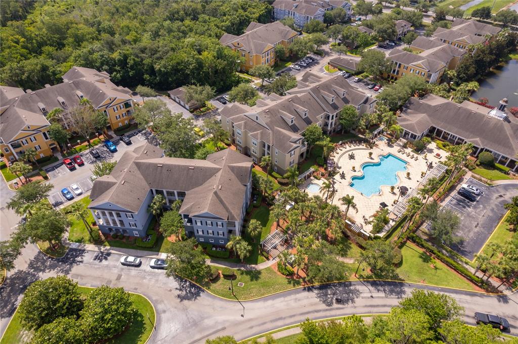 An aerial view shows apartment buildings, a swimming pool, and parking lots surrounded by trees — 3589 CONROY ROAD UNIT 1015, ORLANDO, FL