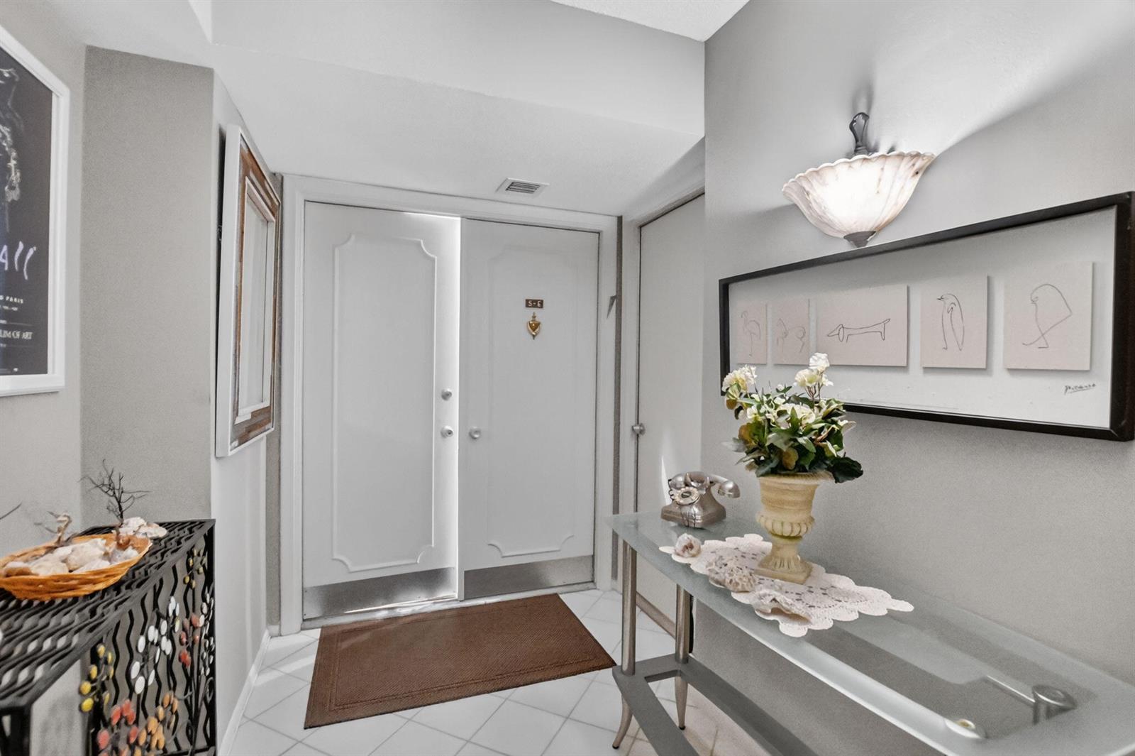 A bright entryway features white double doors, a glass console table, and framed wall art — 1180 S Ocean Boulevard # 0055, Boca Raton FL 33432, BOCA RATON, FL