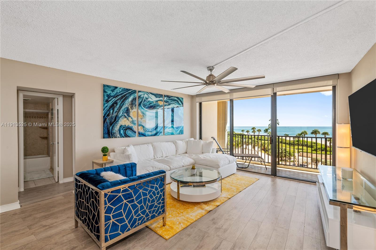 A living room features a white sectional, blue accent chair, yellow rug, and ocean view — 300 Ocean Trail Way # 406, Jupiter FL 33477, JUPITER, FL