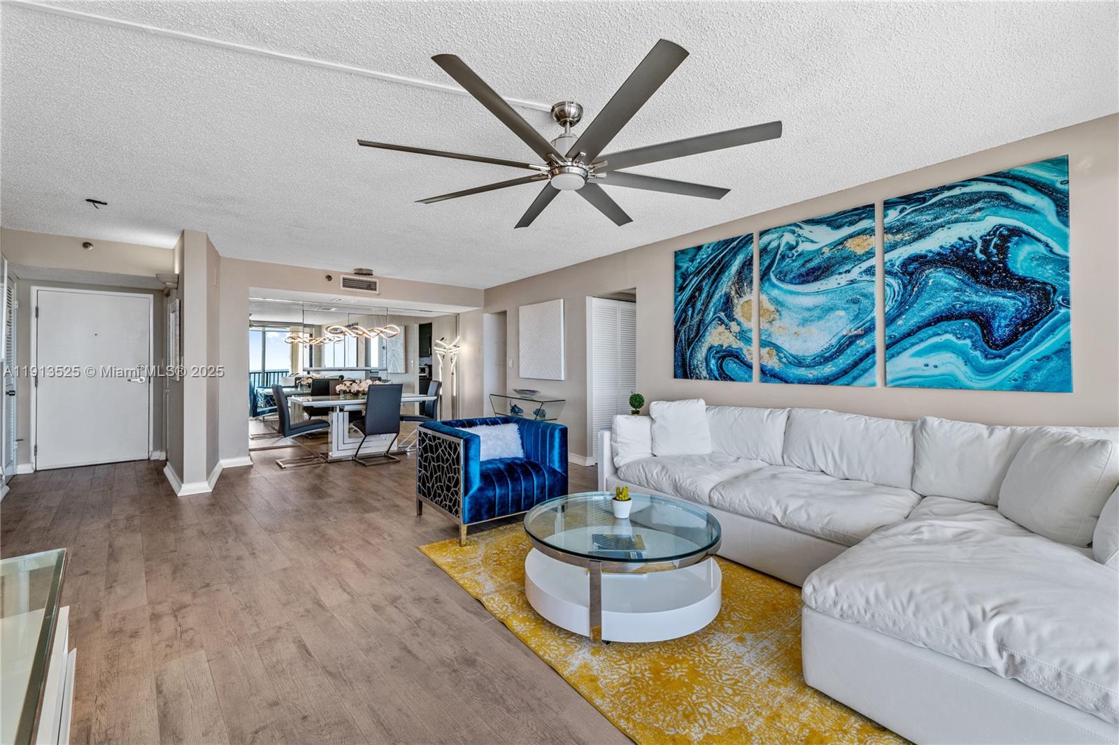 A living room features a white sectional sofa, blue accent chair, and large abstract wall art — 300 Ocean Trail Way # 406, Jupiter FL 33477, JUPITER, FL