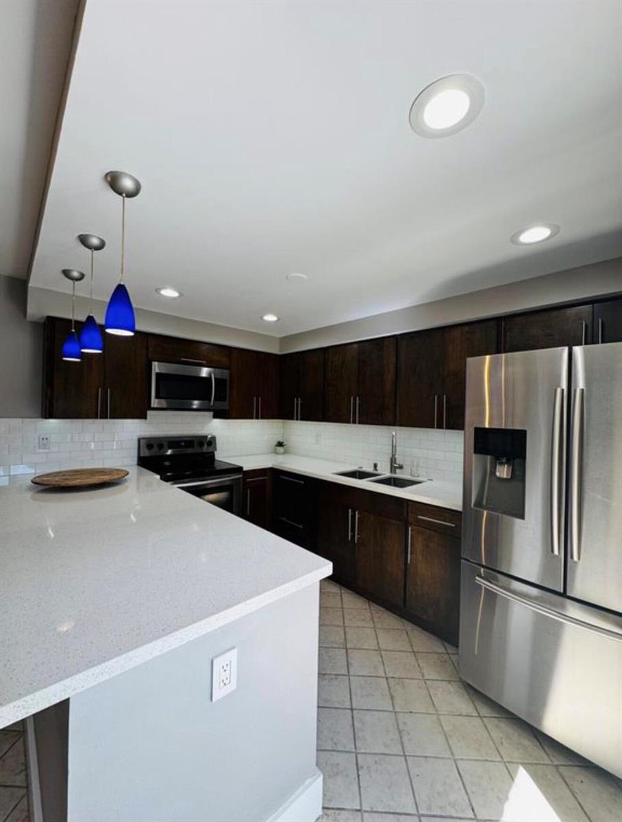 A kitchen features dark wood cabinets, white countertops, stainless steel appliances, and blue pendant lights — 3665 Silver Lace Ln # 77, Boynton Beach FL 33436, BOYNTON BEACH, FL