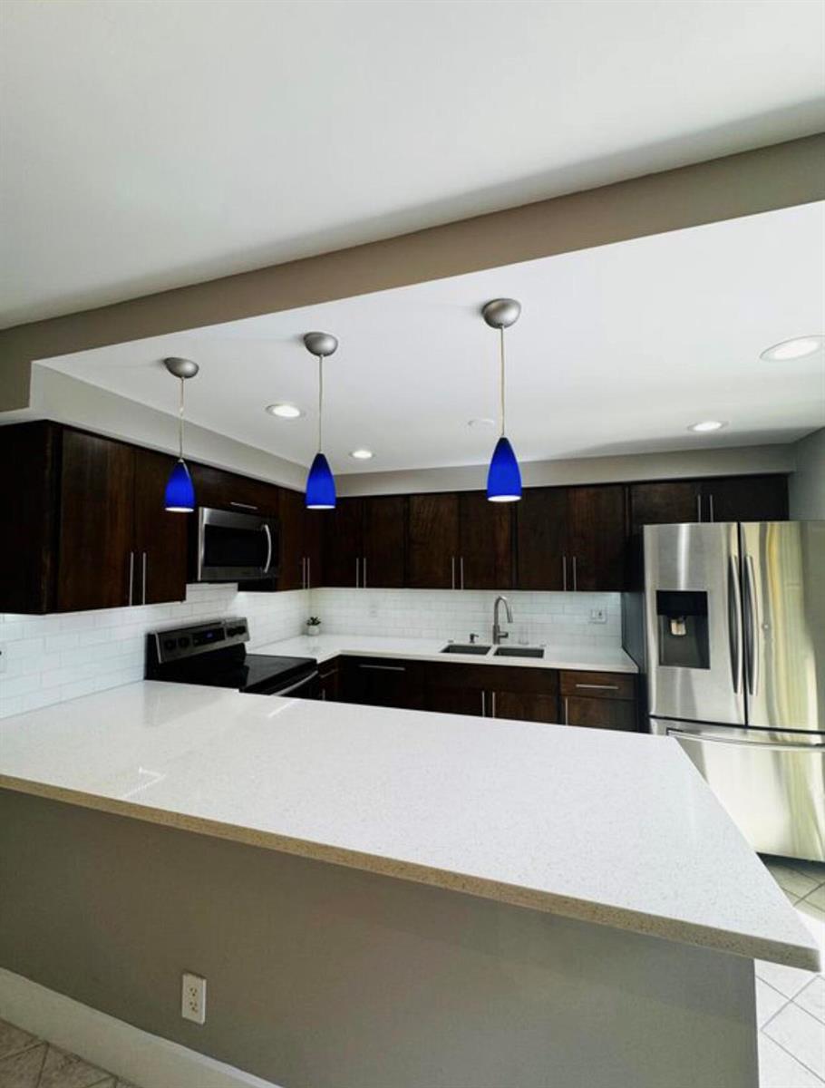 A kitchen with dark wood cabinets, white countertops, a white subway tile backsplash, and blue pendants — 3665 Silver Lace Ln # 77, Boynton Beach FL 33436, BOYNTON BEACH, FL