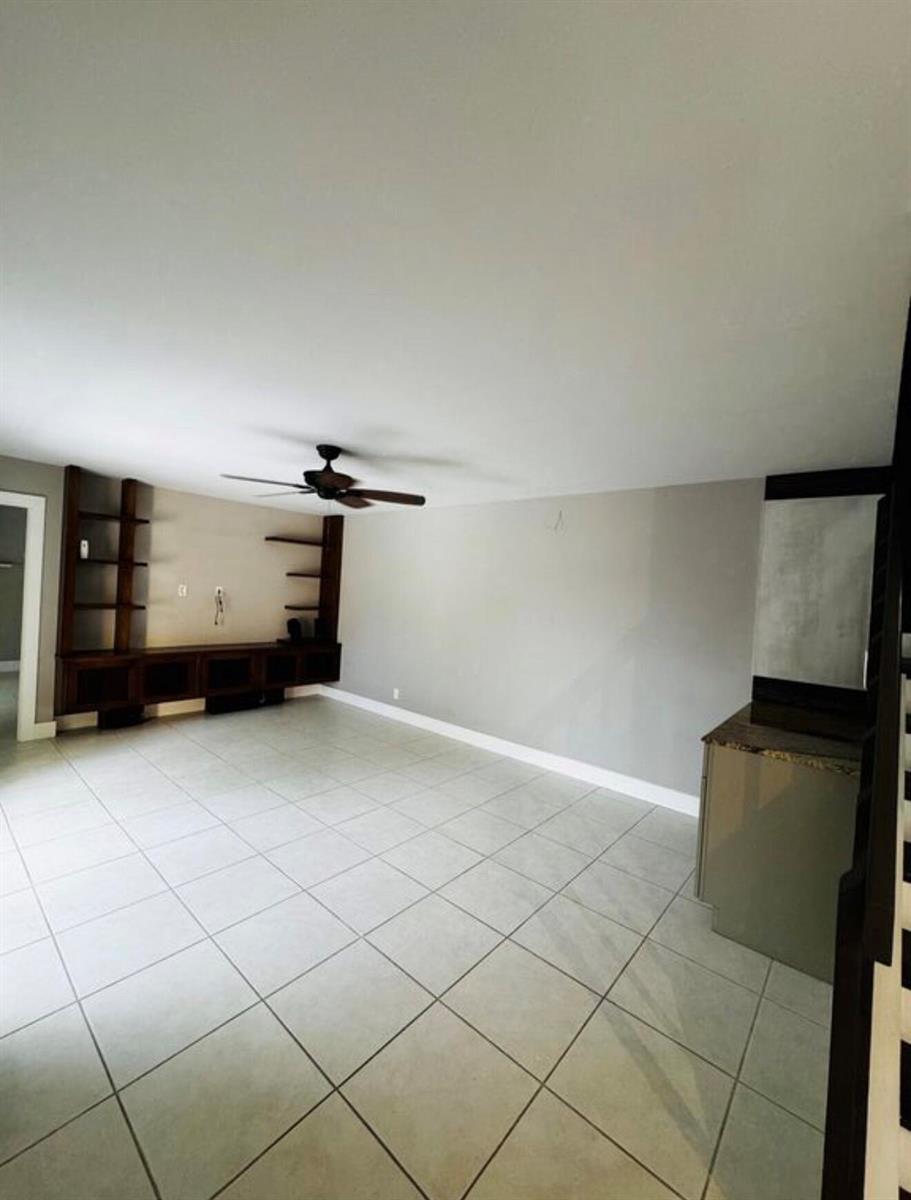 An empty room features light-colored tile flooring, a ceiling fan, and built-in dark wood shelving — 3665 Silver Lace Ln # 77, Boynton Beach FL 33436, BOYNTON BEACH, FL
