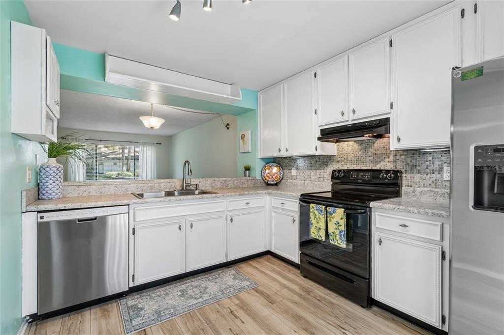 A kitchen features white cabinets, stainless steel appliances, a mosaic backsplash, and light wood flooring — 7803 AMBERLEA COURT, TEMPLE TERRACE, FL