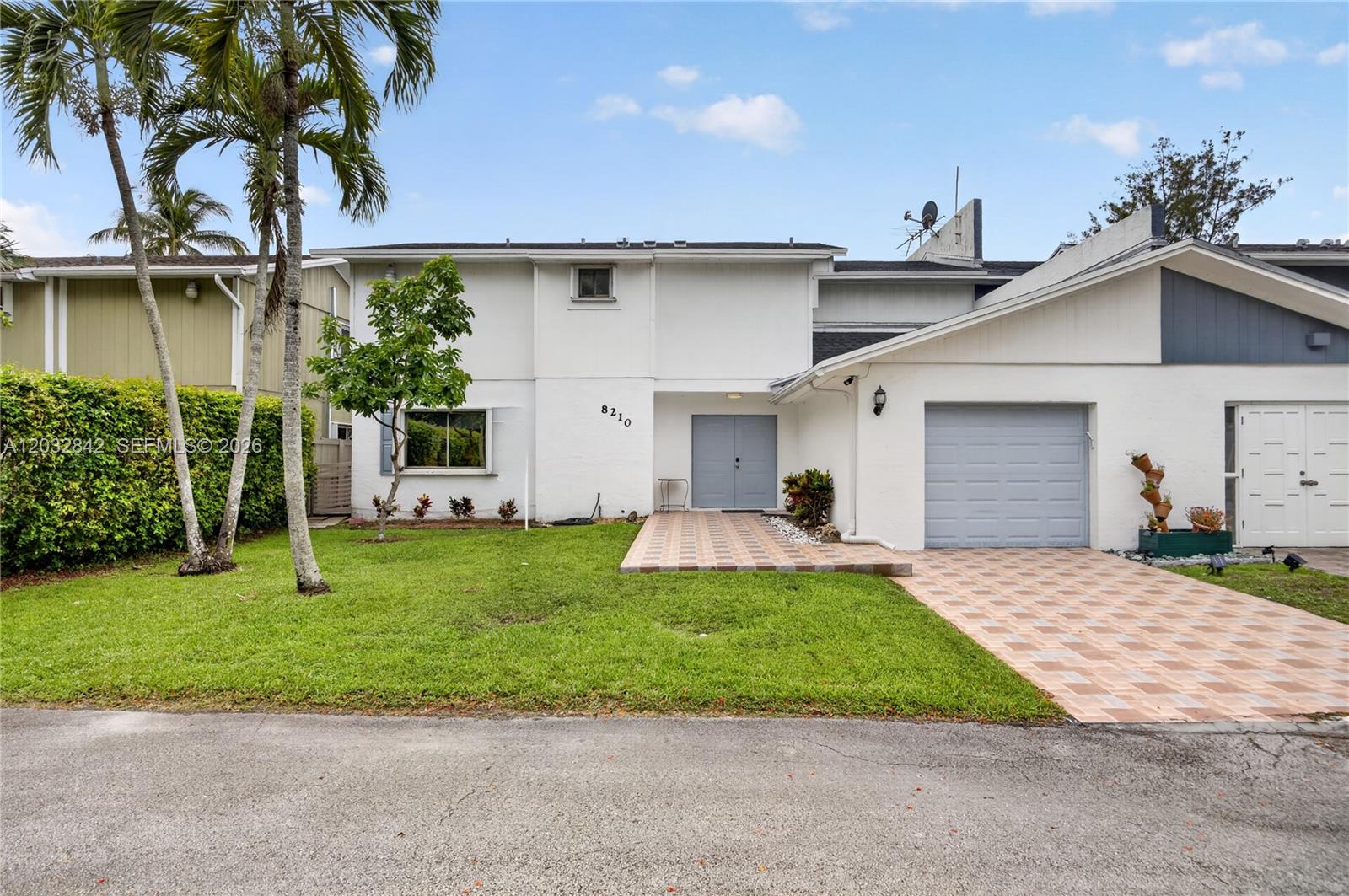 A two-story white house with a gray garage door, tiled driveway, and palm trees — 8210 SW 96th Ct, Miami FL 33173, MIAMI, FL