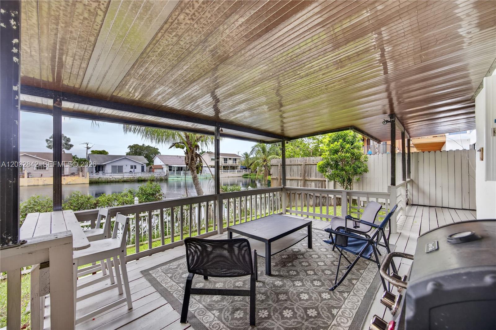 A covered wooden deck overlooks a canal with outdoor furniture and a grill — 8210 SW 96th Ct, Miami FL 33173, MIAMI, FL