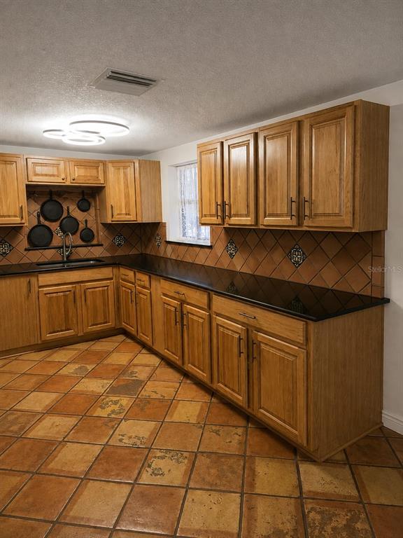 A kitchen features oak cabinets, black countertops, a tiled backsplash, and terracotta floor tiles — 16109 INDIAN MOUND ROAD, TAMPA, FL