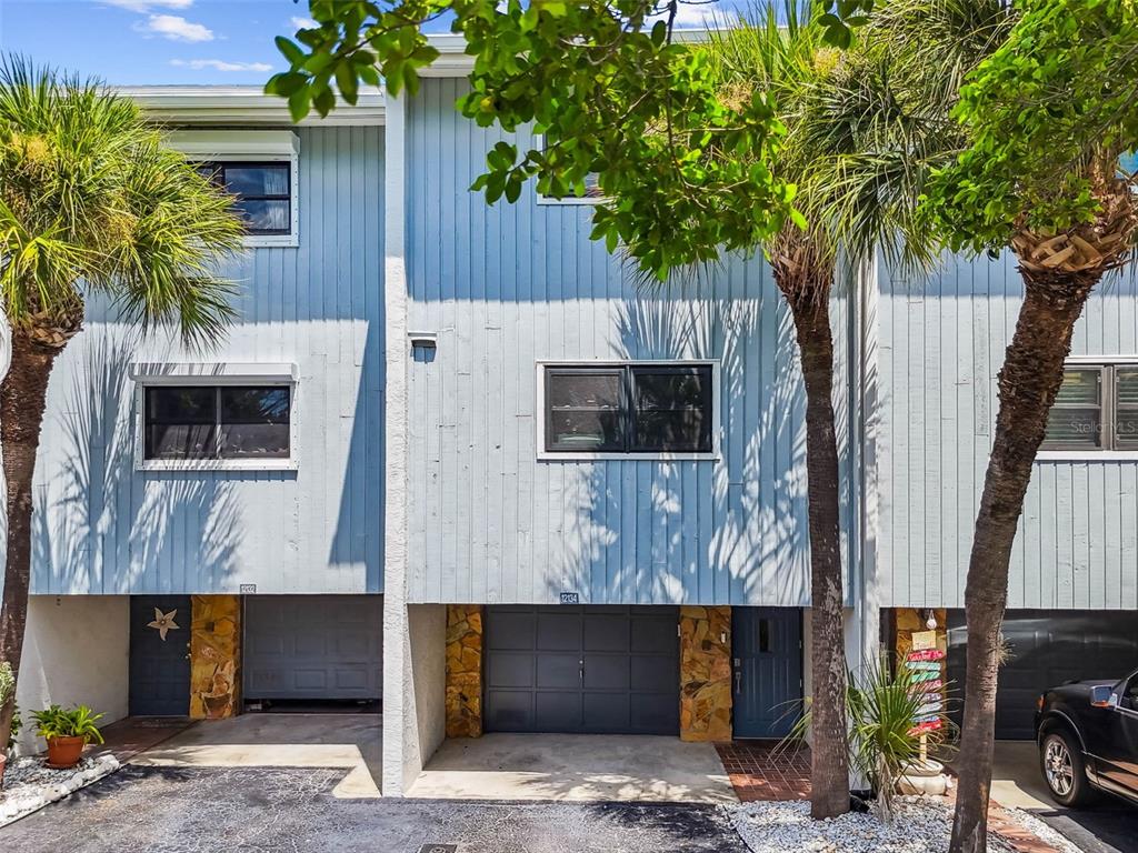 The exterior of a multi-story townhouse features light blue vertical siding, stone accents, and garages — 12134 CAPRI CIR S UNIT 803, TREASURE ISLAND, FL