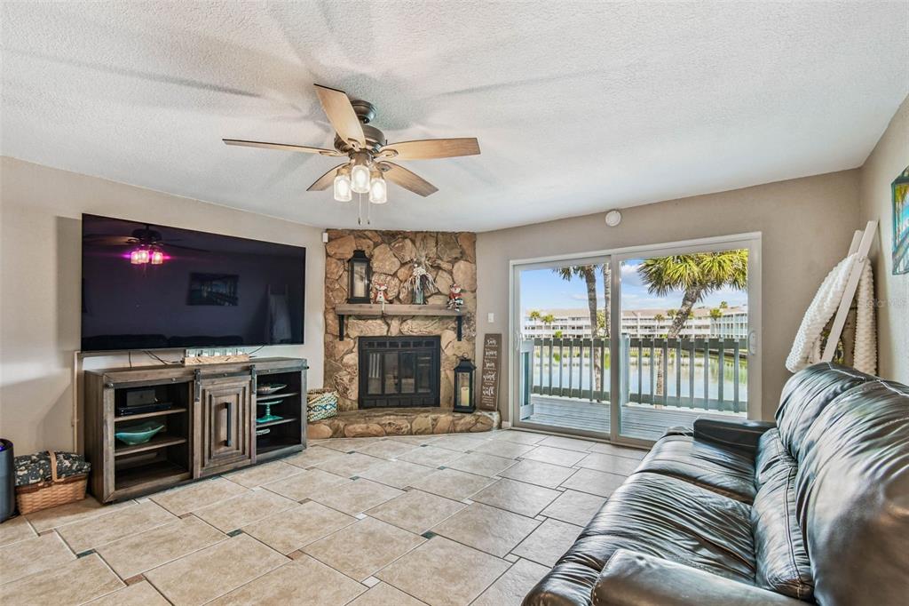 A living room features a stone corner fireplace, tile flooring, and a sliding glass door — 12134 CAPRI CIR S UNIT 803, TREASURE ISLAND, FL