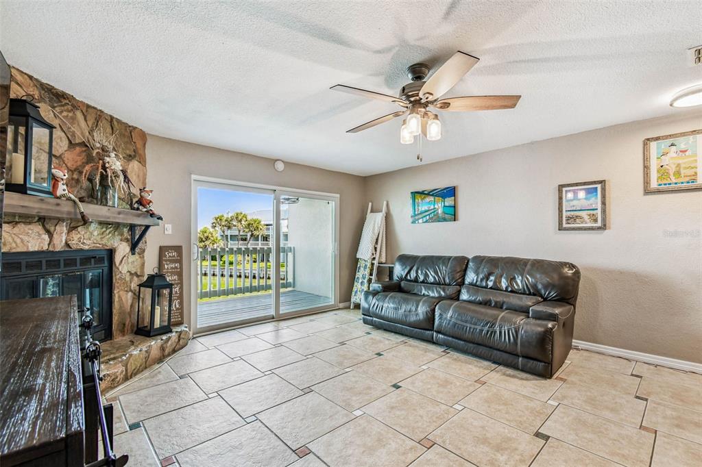 A living room features a stone fireplace, tile flooring, a leather sofa, and sliding glass doors — 12134 CAPRI CIR S UNIT 803, TREASURE ISLAND, FL