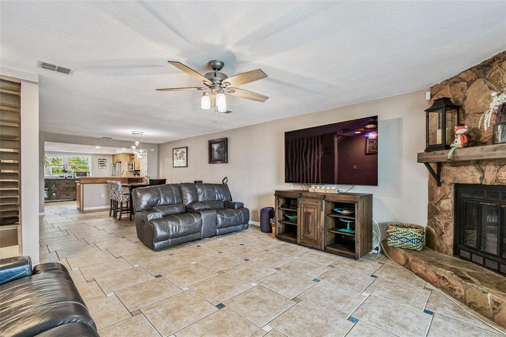A living room with tile flooring, a stone fireplace, a ceiling fan, and a television — 12134 CAPRI CIR S UNIT 803, TREASURE ISLAND, FL