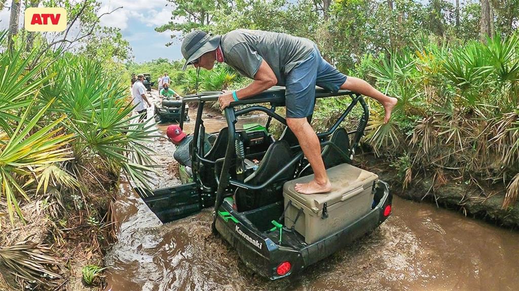A man stands on a cooler in a Kawasaki ATV stuck in a muddy trail — HWY 630 E, FROSTPROOF, FL