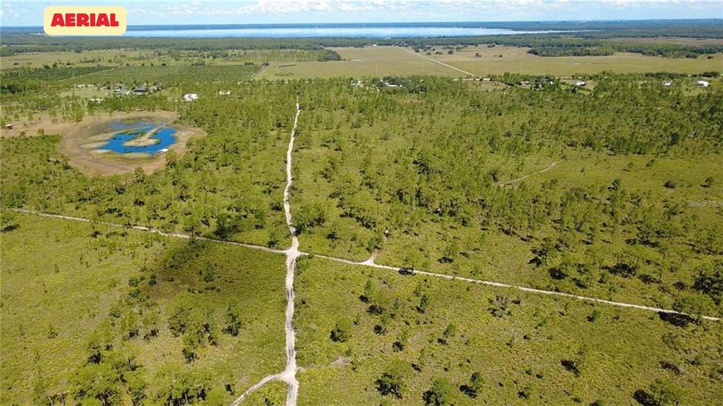 An aerial view shows a large, undeveloped grassy lot with scattered trees and dirt paths — HWY 630 E, FROSTPROOF, FL