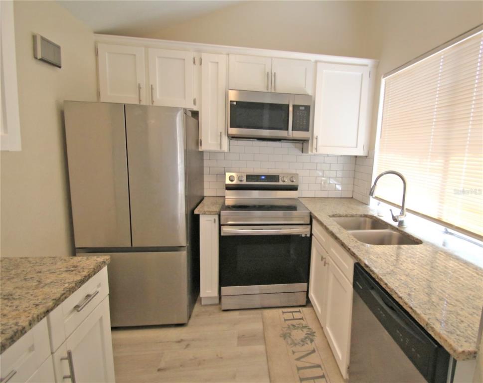 A kitchen features white cabinets, granite countertops, stainless steel appliances, and a subway tile backsplash — 12217 SADDLE STRAP ROW, HUDSON, FL