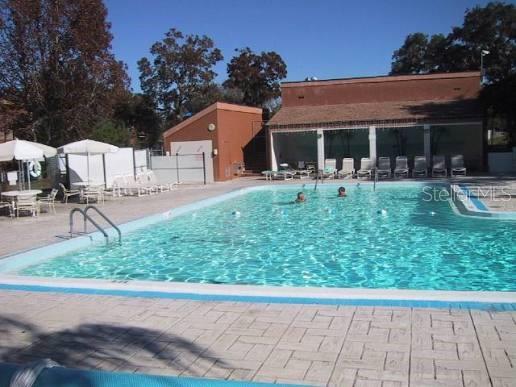 An outdoor swimming pool with lounge chairs and a clubhouse building in the background — 12217 SADDLE STRAP ROW, HUDSON, FL