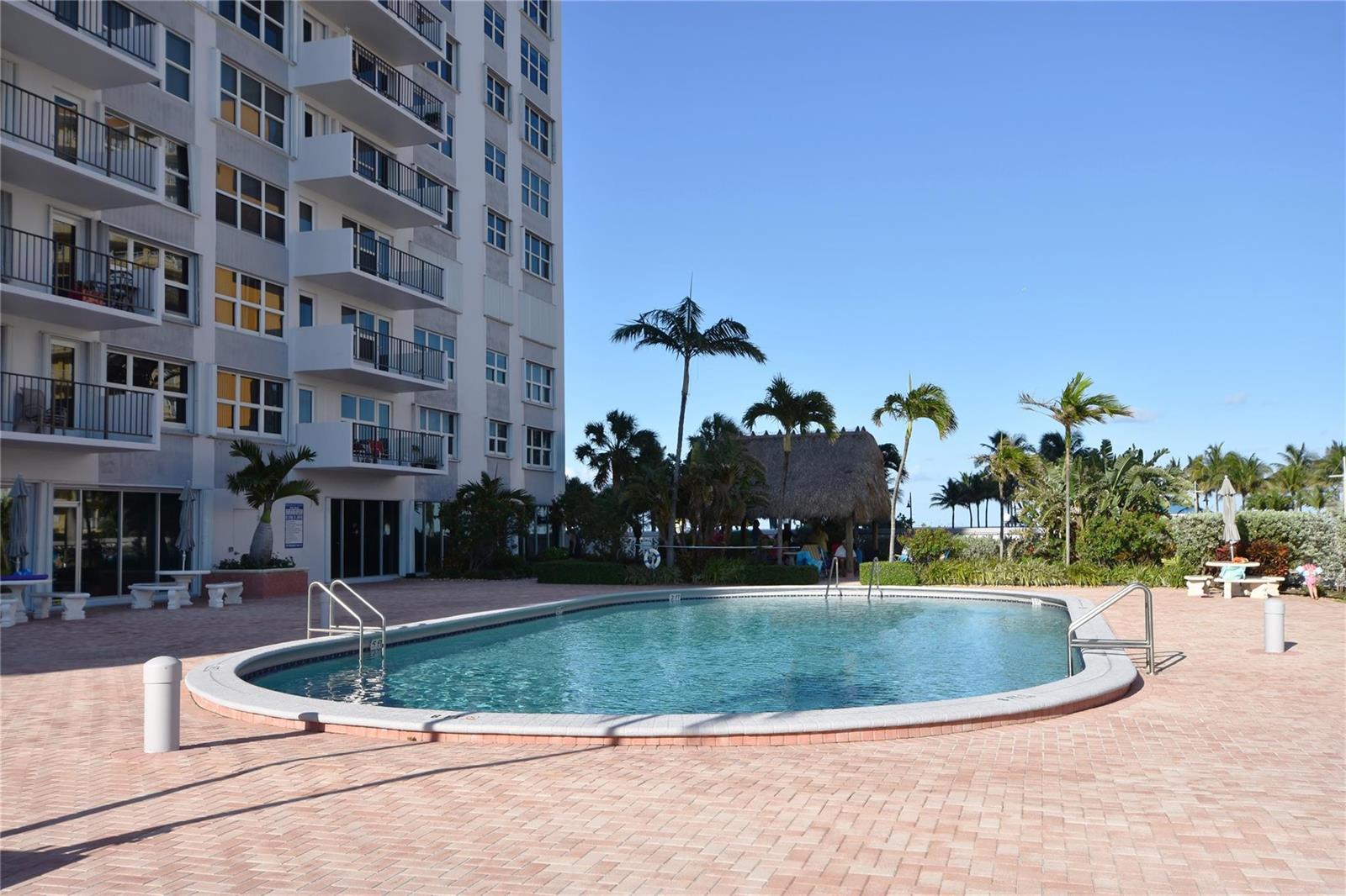 An oval swimming pool sits on a brick patio beside a tall residential building — 405 N Ocean Boulevard # 207, Pompano Beach FL 33062, POMPANO BEACH, FL