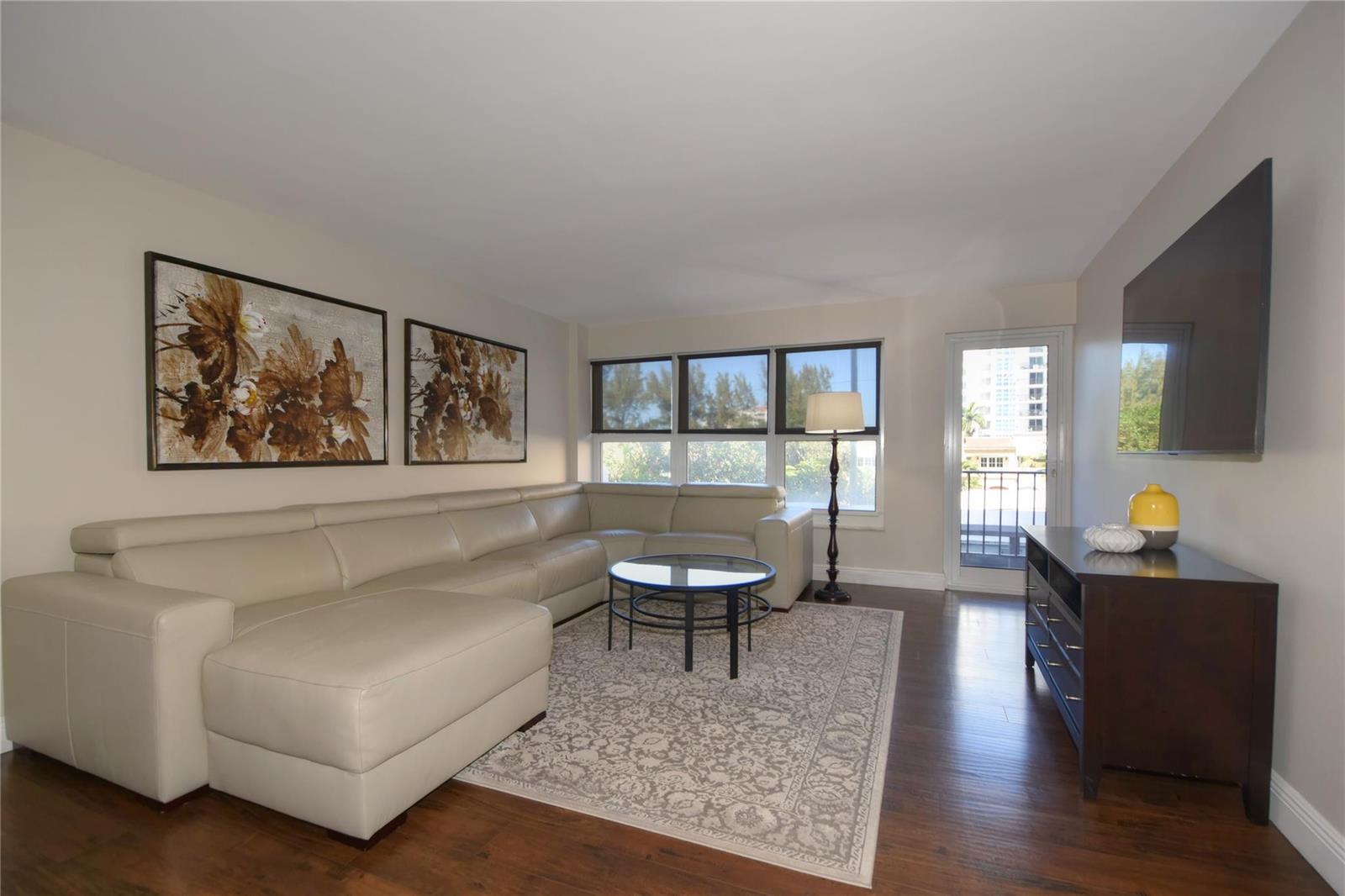 A living room features a beige sectional sofa, a glass coffee table, and dark flooring — 405 N Ocean Boulevard # 207, Pompano Beach FL 33062, POMPANO BEACH, FL