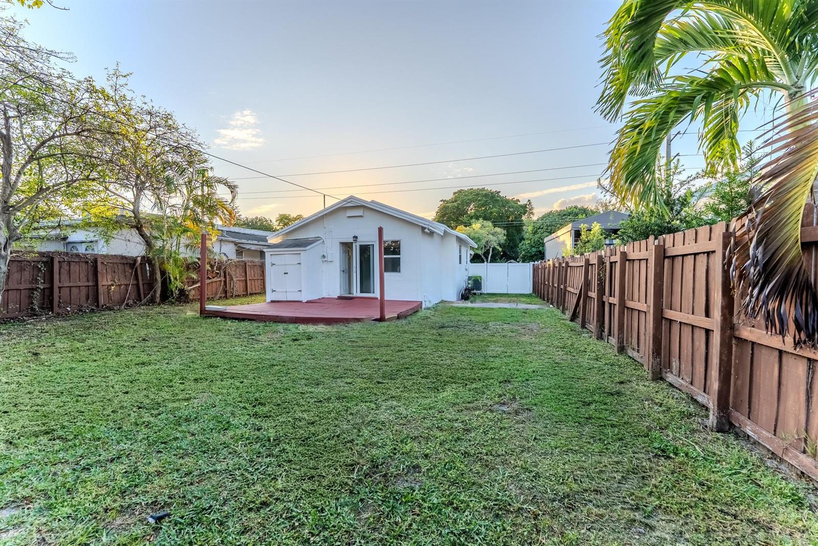 A white house with a red deck sits in a grassy backyard enclosed by fences — 521 S 24th Avenue, Hollywood FL 33020, HOLLYWOOD, FL