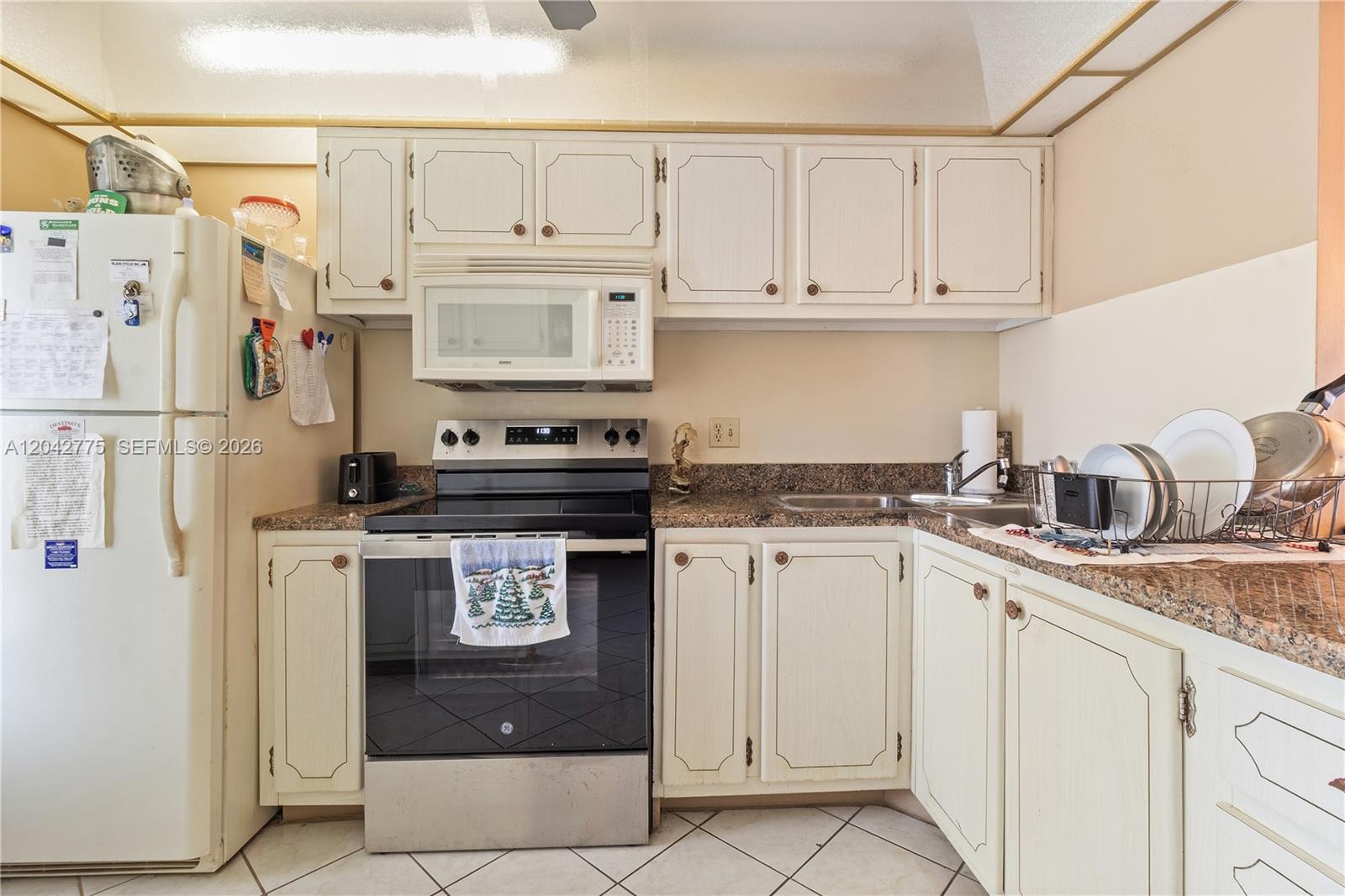 A kitchen features white cabinets, granite countertops, a stainless steel stove, and a white refrigerator — 450 Paradise Isle Blvd # 302, Hallandale Beach FL 33009, HALLANDALE BEACH, FL