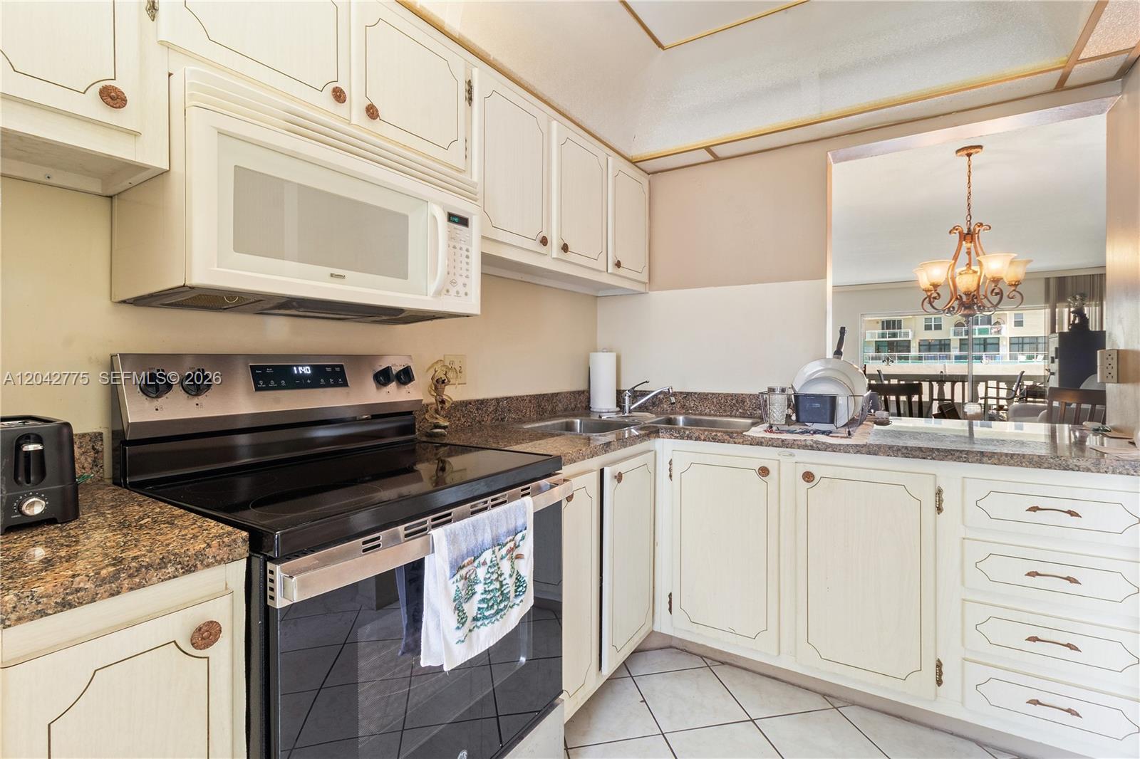 A kitchen features white cabinets, granite countertops, a stainless steel stove, and a pass-through window — 450 Paradise Isle Blvd # 302, Hallandale Beach FL 33009, HALLANDALE BEACH, FL