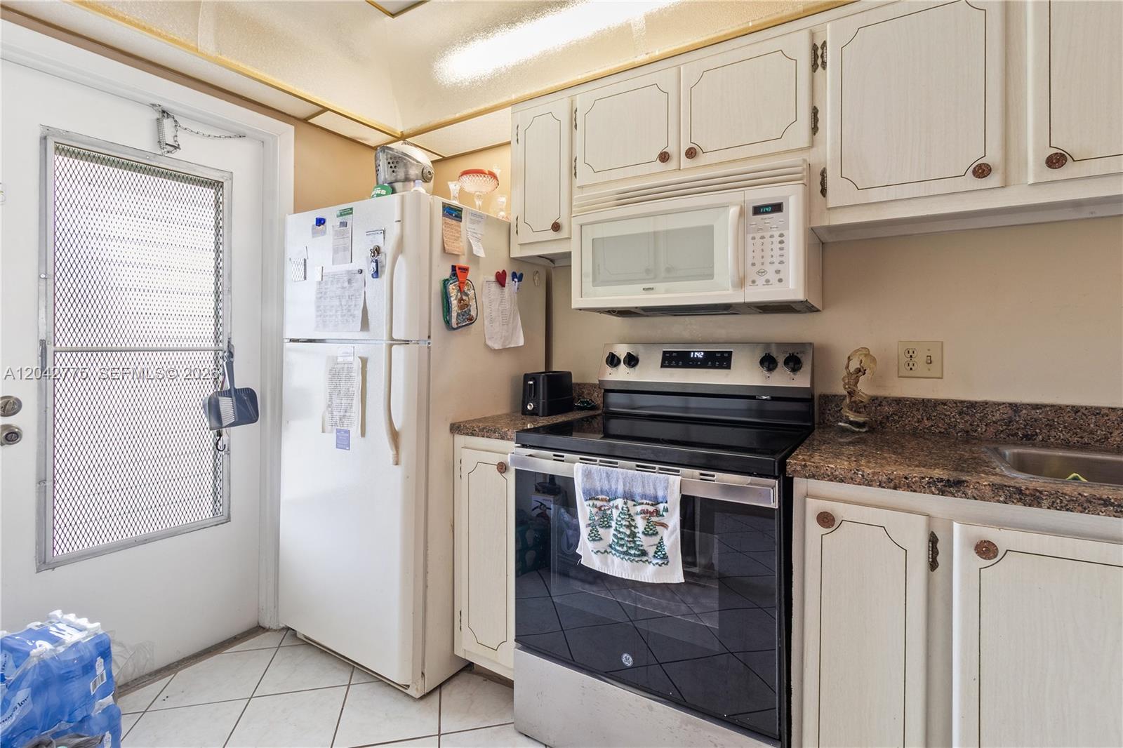 A kitchen features white cabinetry, a stainless steel stove, a white refrigerator, and granite countertops — 450 Paradise Isle Blvd # 302, Hallandale Beach FL 33009, HALLANDALE BEACH, FL