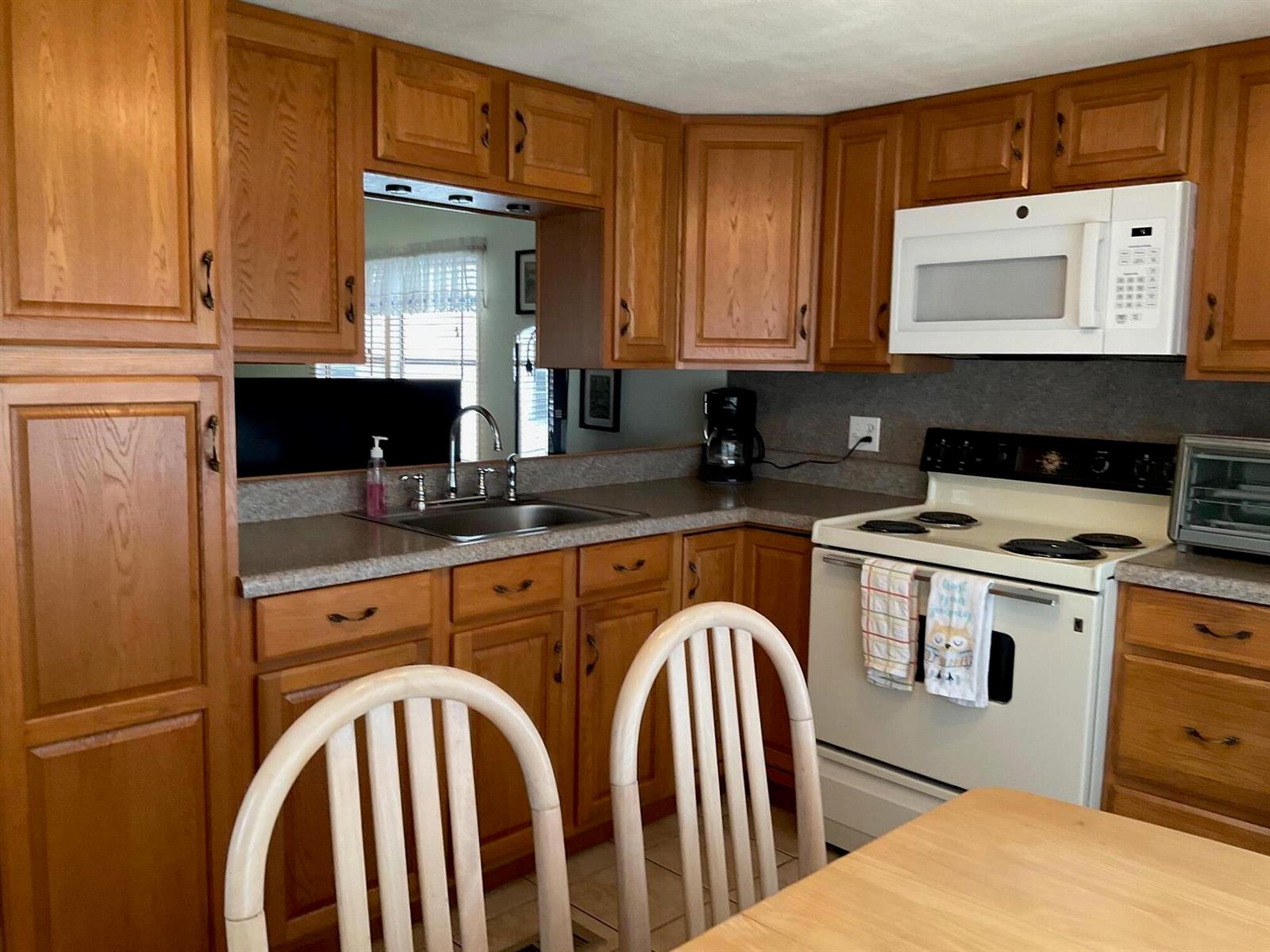 A kitchen features oak cabinets, a white stove, a microwave, and a pass-through window — 1601 Us, Okeechobee FL 34974, OKEECHOBEE, FL